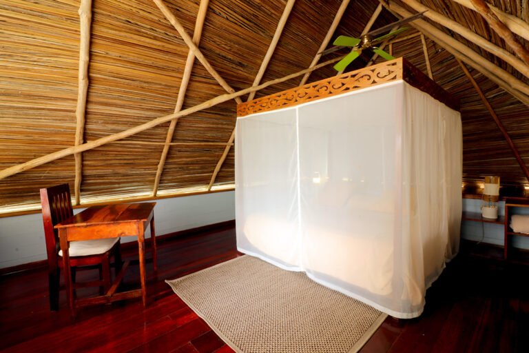 Bedroom under a palm-thatched roof with a bed inside a mosquito net