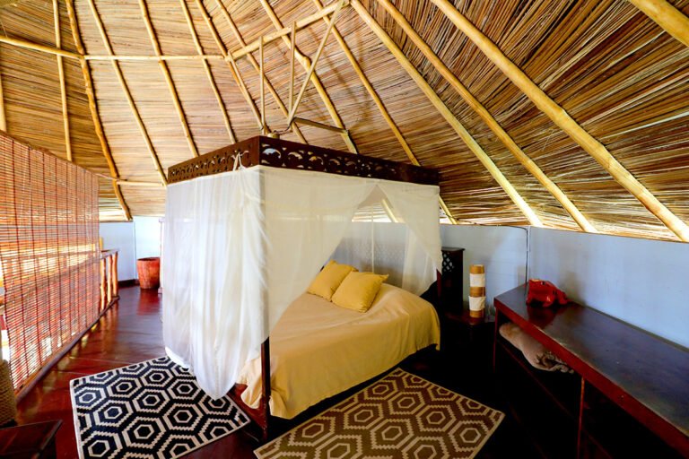 Upstairs bedroom with a mosquito net under the palm-thatched roof
