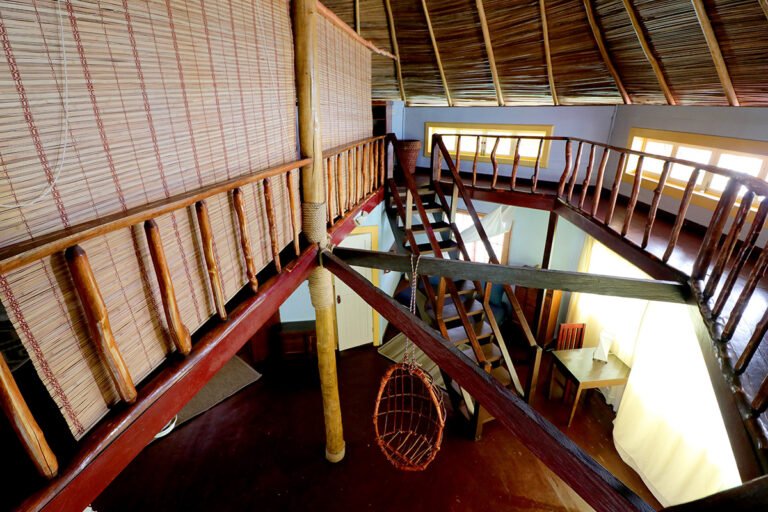Two-level palafito interior with a wooden staircase and thatched roof