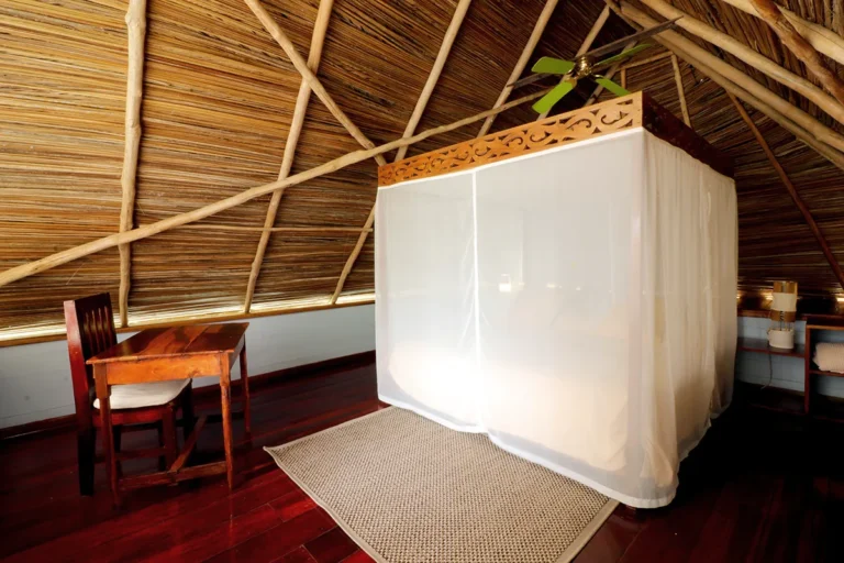 Bedroom under a palm-thatched roof with a bed inside a mosquito net