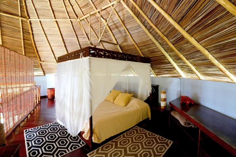 Upstairs bedroom with a mosquito net under the palm-thatched roof