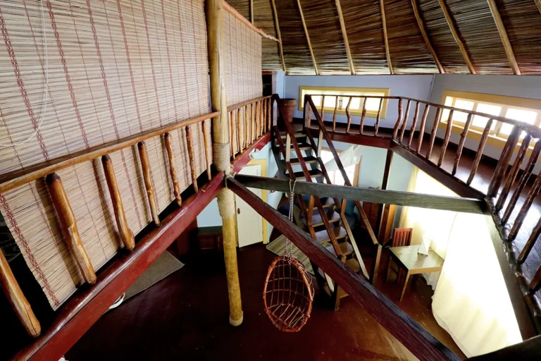 Two-level palafito interior with a wooden staircase and thatched roof