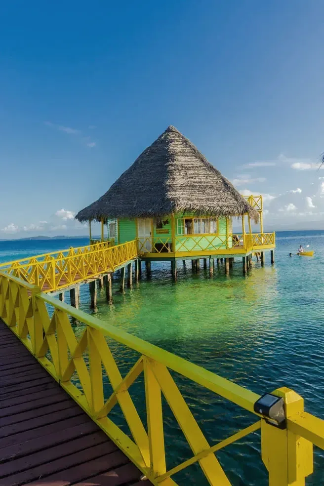 Palafito with palm roof at the end of the walkway over turquoise water