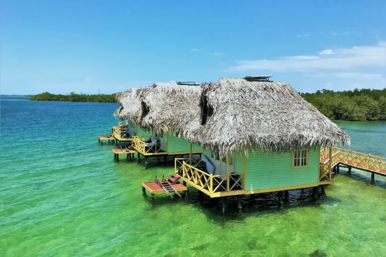 Overwater palafitos on clear green water with mangroves behind