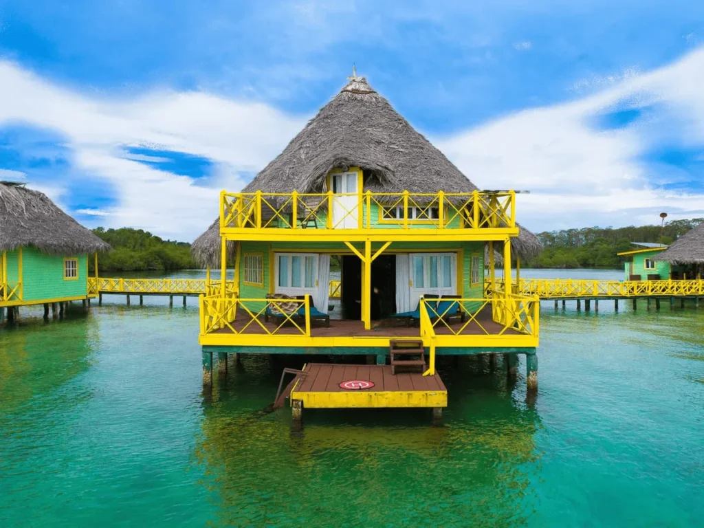 Two-story overwater palafito with yellow railings and a deck at sea level
